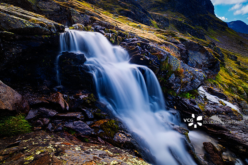雄伟的山间瀑布从覆盖着苔藓的岩石上倾泻而下，映衬着晴朗的蓝天，瑞士达沃斯图片素材