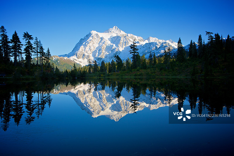 雄伟的雪山倒映在宁静的湖面上，蓝天清澈，位于美国斯诺夸尔米国家森林。图片素材