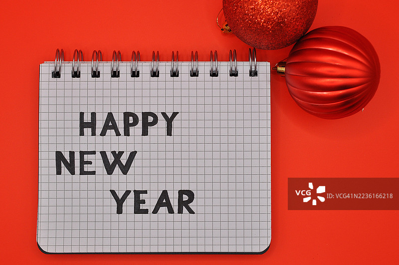 红色背景上有红色圣诞装饰的记事本上的新年快乐祝福信息图片素材