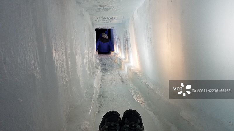 一个人站在冰洞内湿滑的冰面上，低角度拍摄，望向远处的另一个人。图片素材