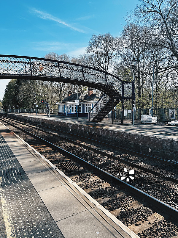 阳光明媚的日子，空荡荡的铁路站台和轨道，背景中有一座人行天桥和车站建筑，皮特洛赫里，英国图片素材
