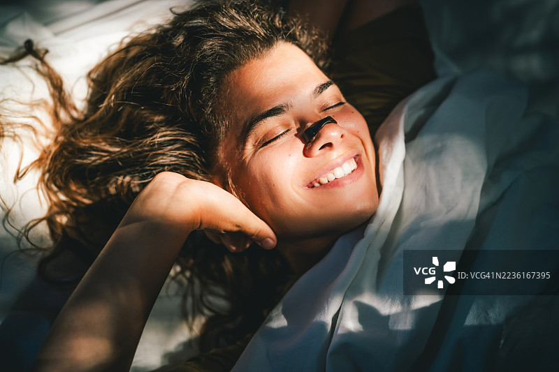 年轻女性躺在床上，鼻子上贴着磁性呼吸条，象征着现代健康、呼吸支持和创新健康科技，以改善呼吸和睡眠。图片素材