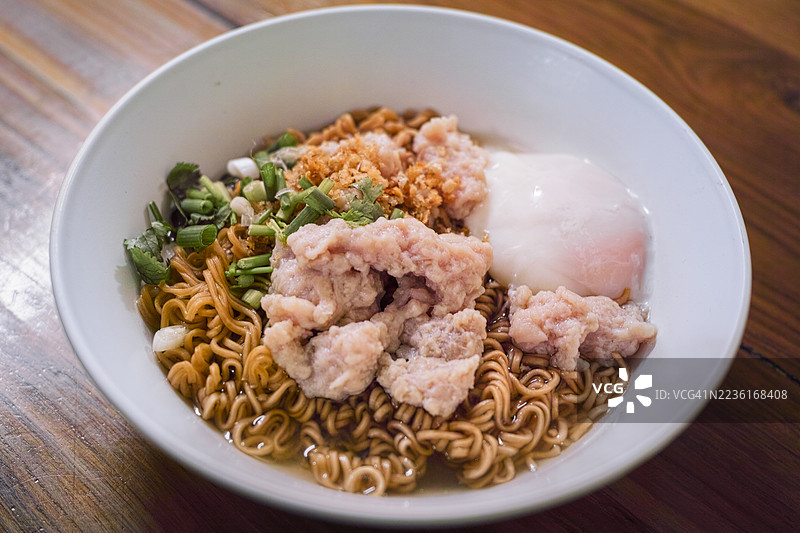 高角度视图的木桌上放着一碗方便面，配有剁碎的猪肉、鸡蛋和葱。图片素材