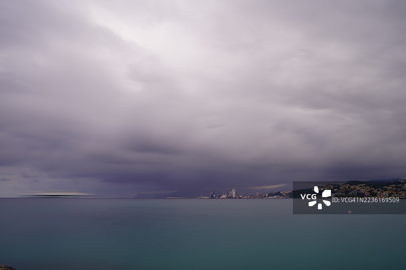 戏剧性的暴风云在宁静的海面上聚集，远处是海岸线，意大利阿尔比索拉·苏佩里奥雷图片素材