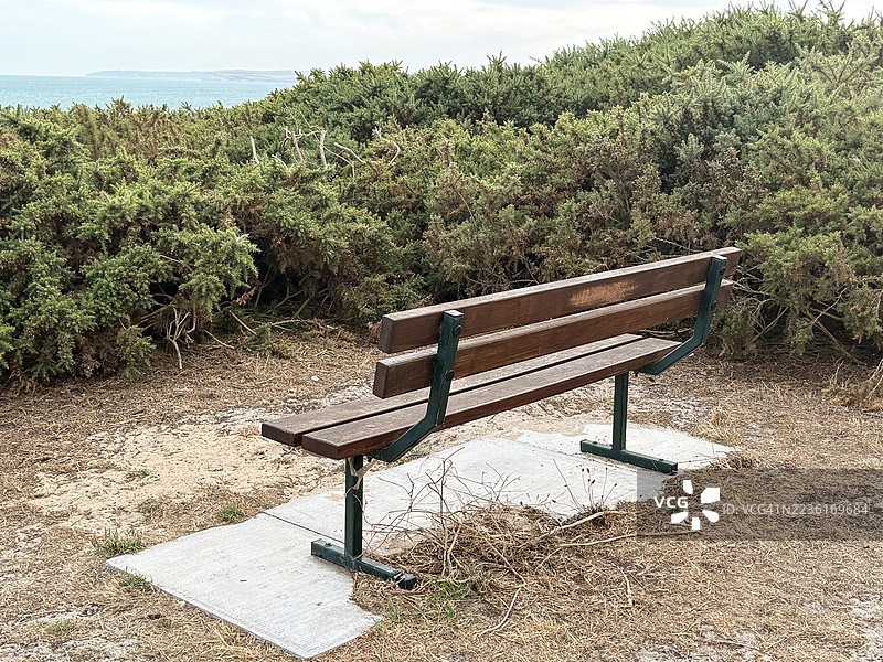 空荡荡的木长椅俯瞰大海，四周被绿色灌木环绕，位于一个阴云密布的海滨公园中。图片素材