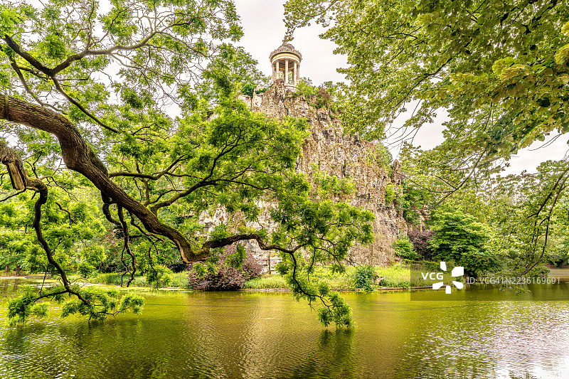 湖泊的美丽景色，郁郁葱葱的树木和一座经典的凉亭坐落在岩石突起上，映衬着明亮的天空。图片素材