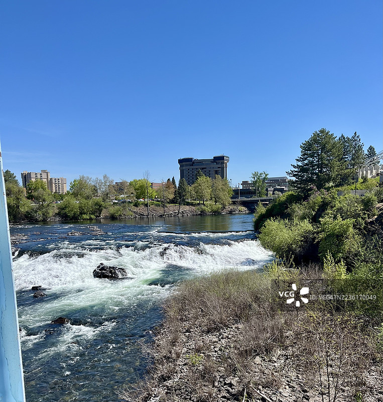 清澈蓝天下，城市天际线旁的河流急流美景图片素材