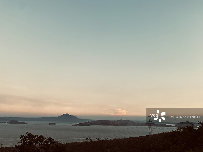 宁静的日落映照在辽阔的湖面上，远处有岛屿和山脉，天空呈现渐变色彩。图片素材