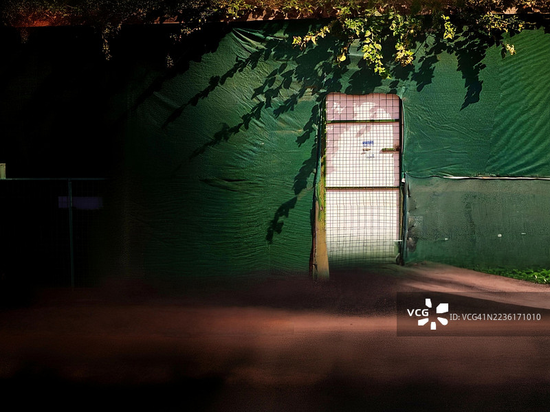 阳光和阴影洒在绿色施工围栏和金属大门上，伊尔比勒，伊拉克图片素材