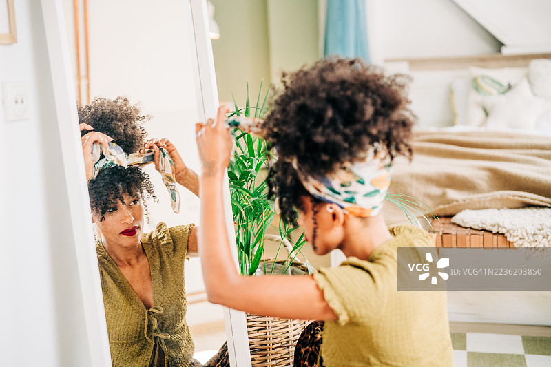 一位女性在镜子前整理她的卷发。图片素材