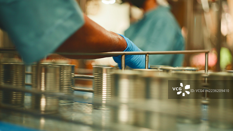 传送带上的罐装鱼，背景是正在准备罐头食品的工人。图片素材