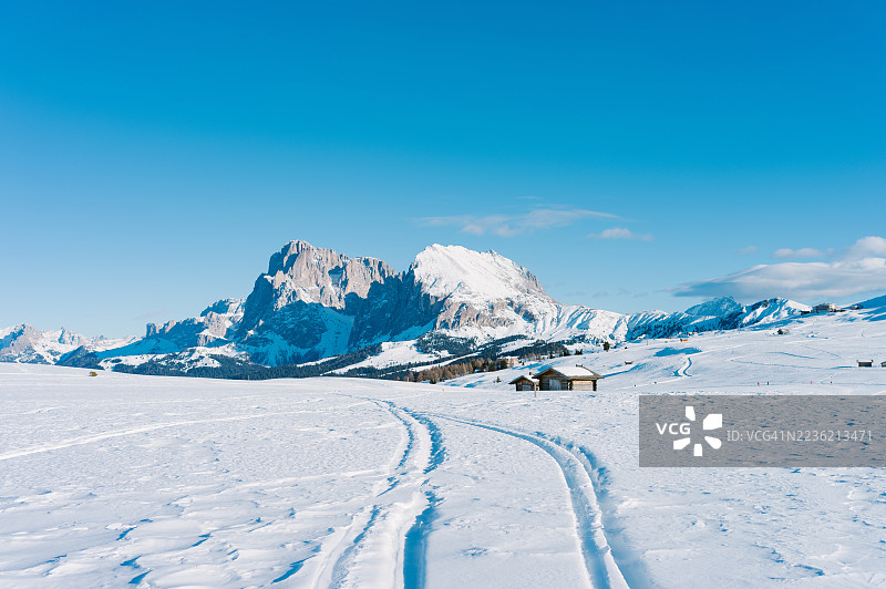 滑雪轨迹通向雪山景观中的小木屋，阳光明媚。图片素材