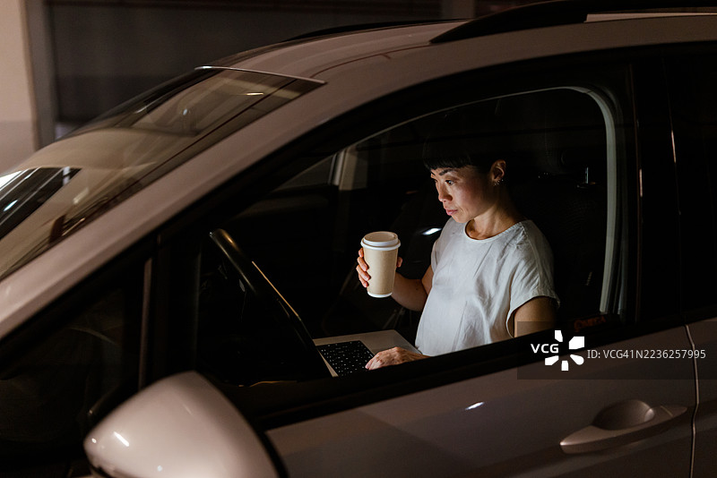 专注的司机在停放的车辆中一边使用笔记本电脑一边喝饮料图片素材