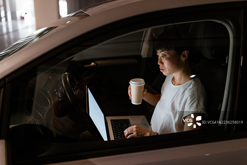 日本女性在车内使用笔记本电脑，同时手里拿着咖啡杯。图片素材