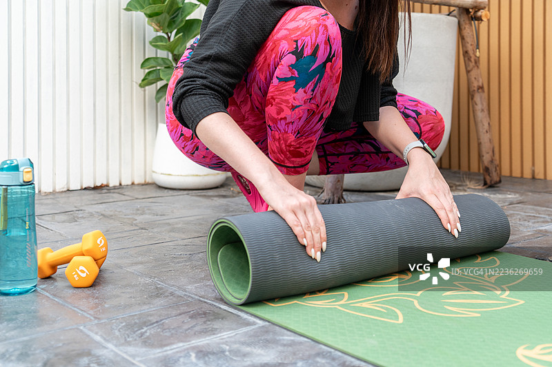 年轻快乐的胖女人在家做运动，手里拿着瑜伽垫和哑铃，旁边有健身球。大码超重女孩看着镜头微笑。锻炼运动概念。图片素材