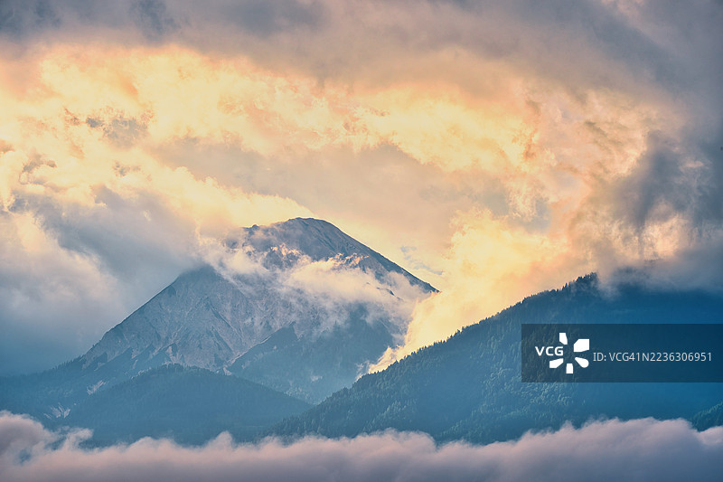 奥地利菲拉赫，壮丽的山脉笼罩在云雾之中，夕阳戏剧性地落下图片素材