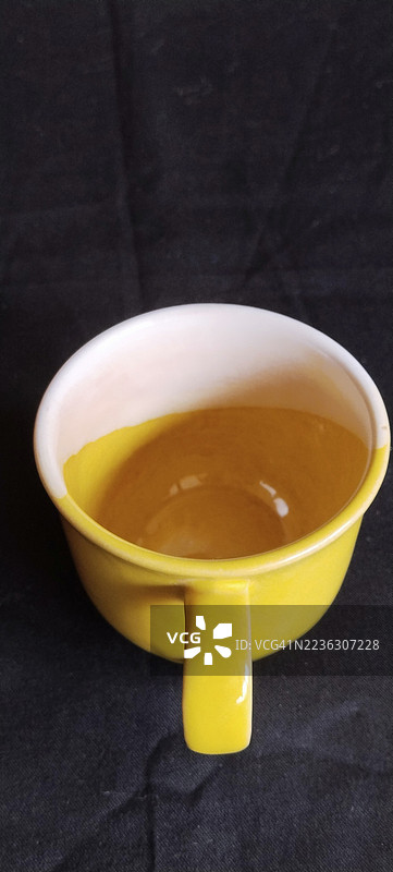 高角度视图的鲜艳黄色茶杯放在深色表面上图片素材