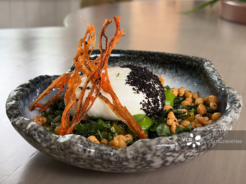 艺术碗中盛放的美食特写，包含软奶酪、脆脆的元素和绿色蔬菜，摆放在桌子上。图片素材