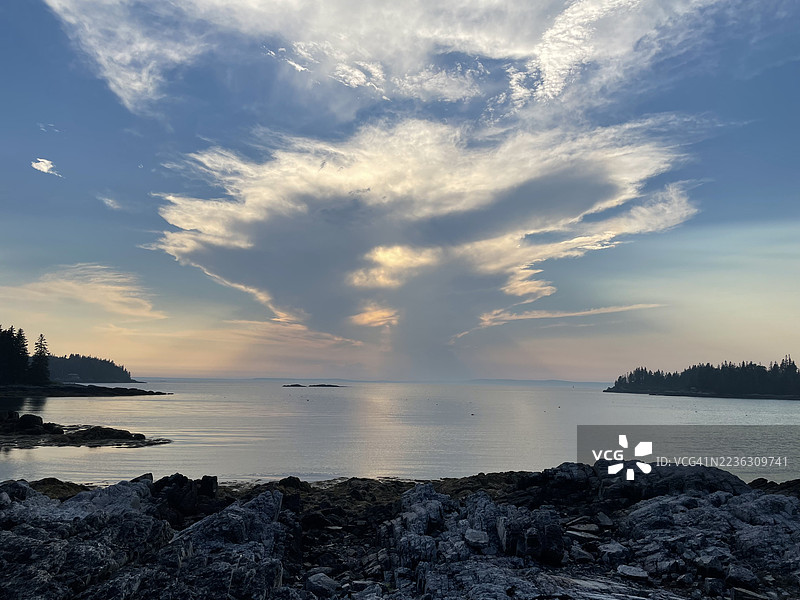 日落时分，宁静海面上方的戏剧性云彩，岩石海岸和远处的岛屿。图片素材