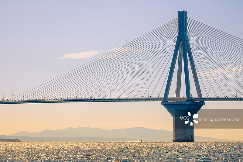 壮观的悬索桥横跨闪耀的水面，背景是日落时分的山脉。图片素材