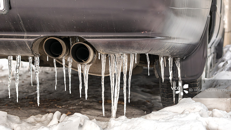 冬季汽车排气管和保险杠上挂着的冰柱特写，地面上覆盖着雪。图片素材