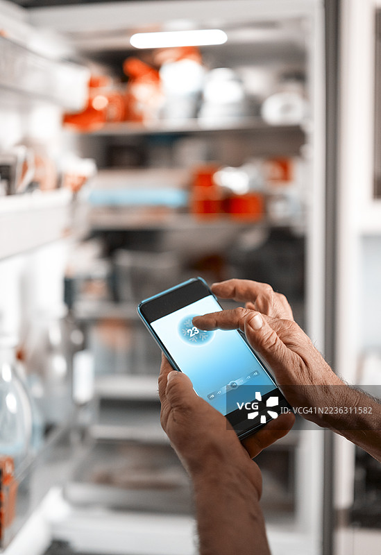 一名男子的手部特写，正在使用手机控制智能冰箱图片素材