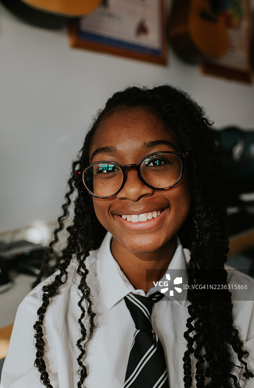 在学校的一天里，一位戴眼镜的年轻女孩学生在音乐教室微笑的肖像。图片素材