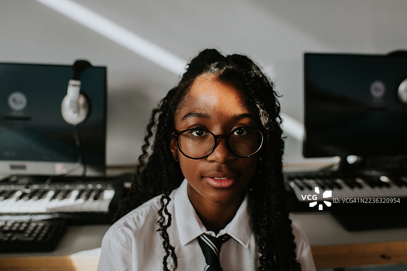 在学校的一天里，戴着眼镜的年轻女孩学生在音乐教室微笑的肖像图片素材