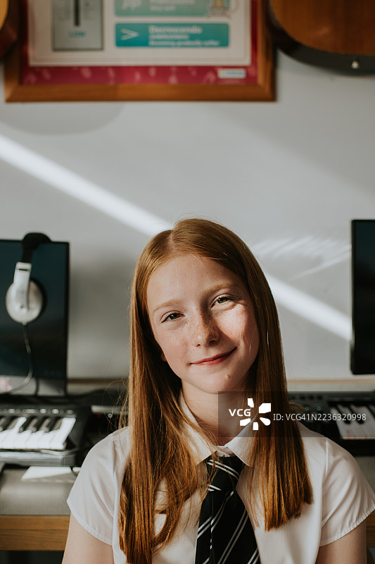 在学校的一天里，姜色头发的年轻女孩学生在音乐教室微笑的肖像图片素材