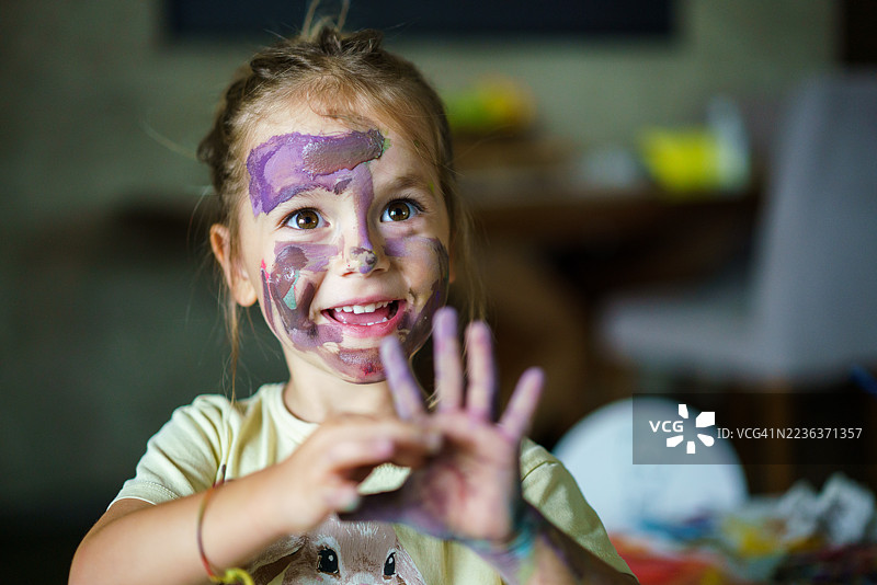 小女孩展示着沾满颜料的手和快乐的脸庞。图片素材