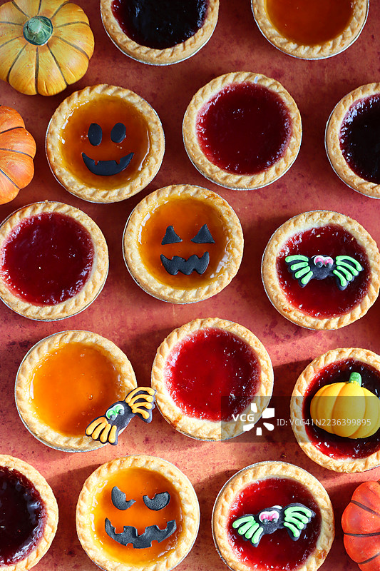 万圣节派对食品的全景图， assorted jam tarts，各种果酱挞，短酥皮甜派，内馅为黑加仑和苹果、草莓或杏子果酱，南瓜灯脸，蜘蛛和南瓜翻糖装饰，橙色背景，俯视图图片素材