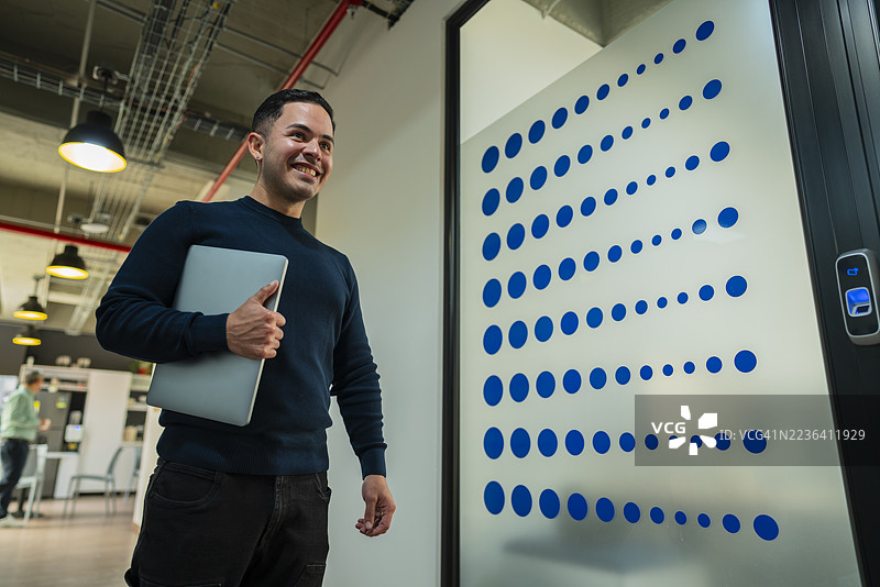 一位行政人员手持笔记本电脑走在办公室走廊上，前往会议。图片素材