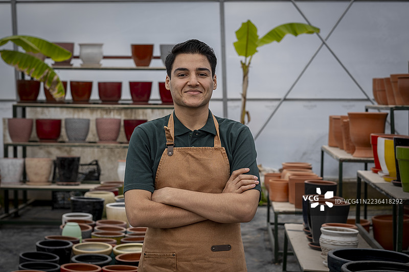自信的温室主人双臂交叉，站在花盆中间图片素材