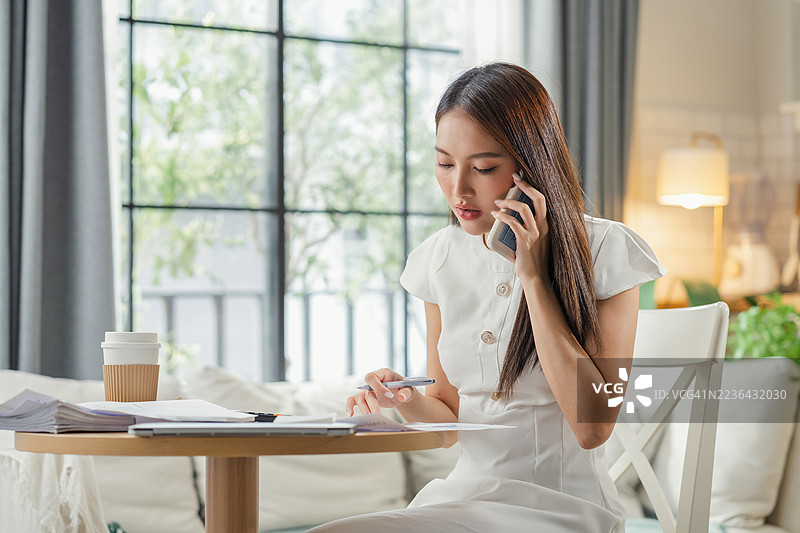 女性企业主在家办公时使用智能手机咨询财务顾问，同时利用人工智能辅助进行财务分析和战略创业规划解决方案。图片素材