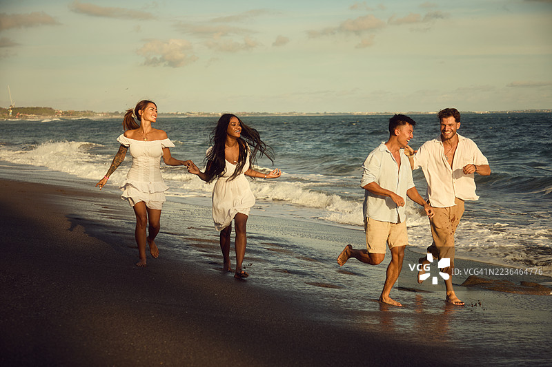 快乐的朋友们在日落时分沿着海滩奔跑，享受无忧无虑的夏日时光图片素材