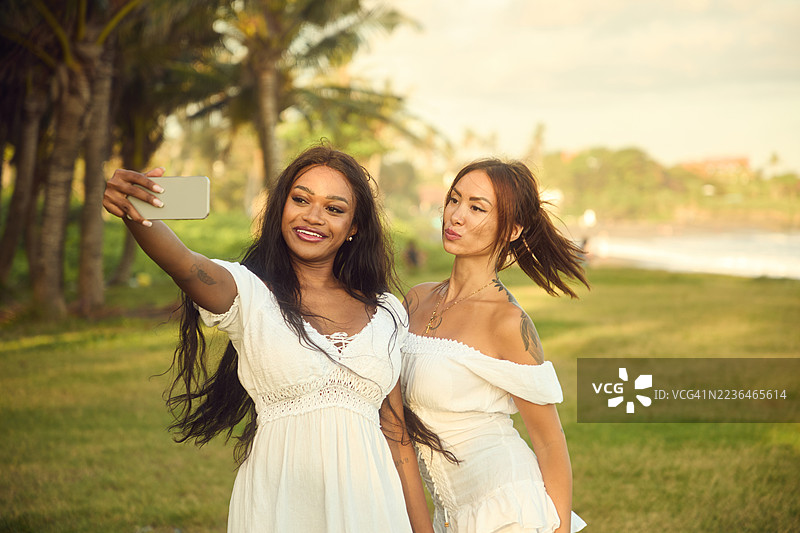 两个朋友在热带公园的阳光下穿着白色裙子自拍图片素材