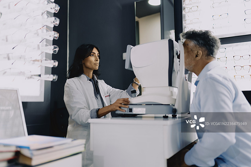 女眼科医生在现代眼科诊所使用诊断设备为老年男性患者进行眼部检查。图片素材