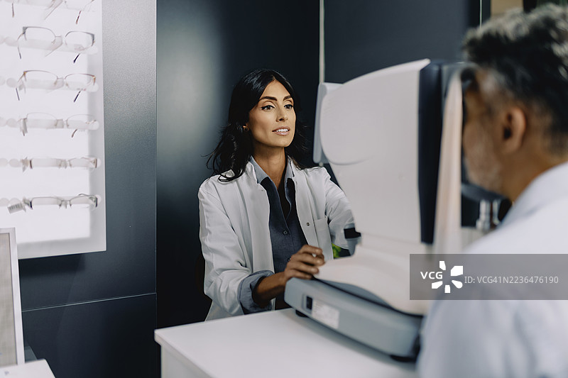 女性眼科医生在现代眼科诊所使用诊断设备为老年男性患者进行眼部检查。图片素材