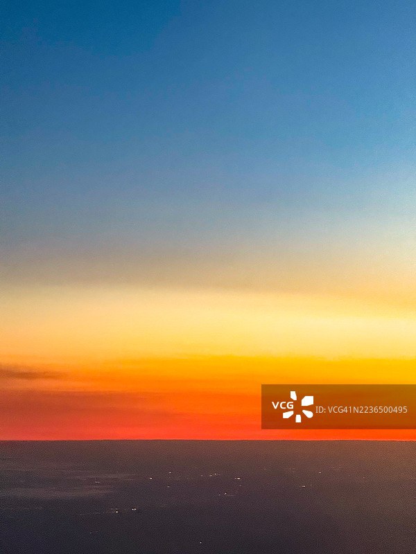 从飞机窗户看到的日落景色，天空从蓝色渐变到金色、红色和深蓝色，底部隐约可见新泽西州的高速公路灯光，拍摄于2025年9月9日。图片素材