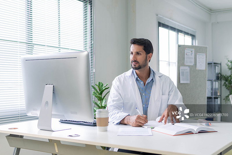 一位专注的拉丁裔研究人员身穿实验服，在现代工作空间中分析数据图片素材