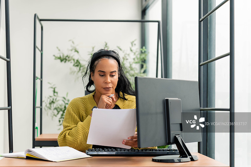 一位专注的非洲裔美国研究员正在她的现代化工作站上查阅文件图片素材