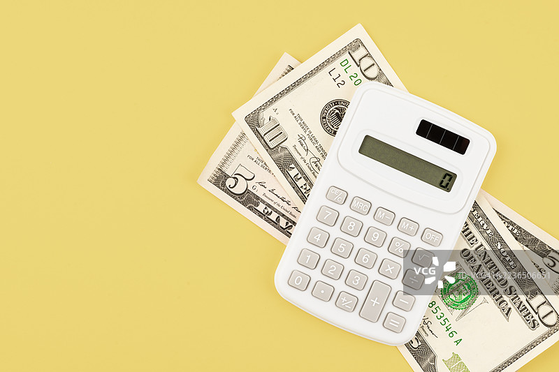 一台计算器放在美元钞票上，背景为黄色，位置留有空白。图片素材