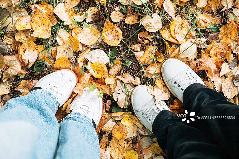 公园里两位年轻朋友的脚踩在黄色秋叶的地毯上俯视图图片素材