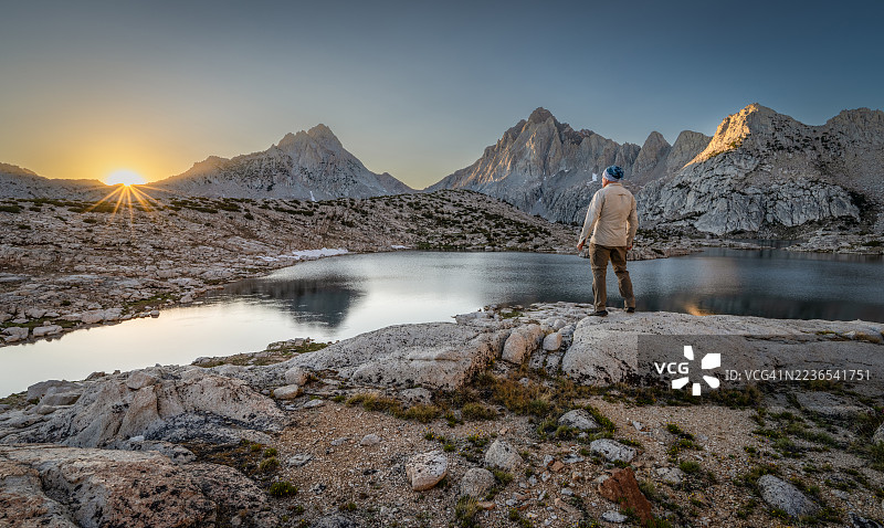 清晨，一名男子背对着镜头站在岩石上，凝视着加利福尼亚州塞拉国家森林的格里内尔湖和内华达山脉。图片素材