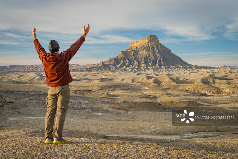一名男子背对着镜头，双臂高举，站在犹他州韦恩县的上蓝山工厂布特前。图片素材