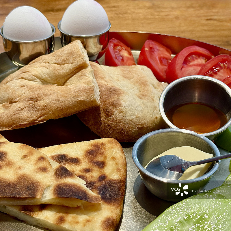 传统格鲁吉亚早餐的特写，包括格鲁吉亚伊梅鲁利哈恰普里、软煮蛋、面包、西红柿、黄瓜、黄油和蜂蜜。图片素材