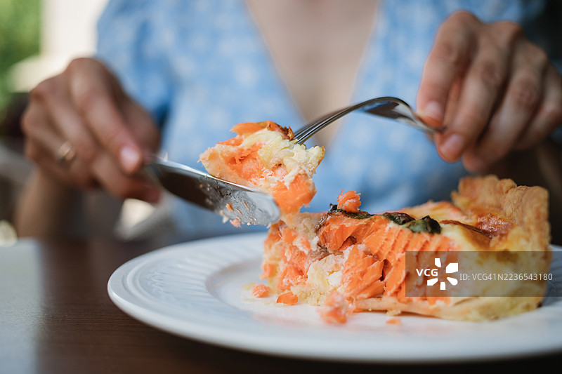 一位穿着夏季连衣裙的女性在户外咖啡馆里享用一片三文鱼咸派作为午餐的特写镜头图片素材