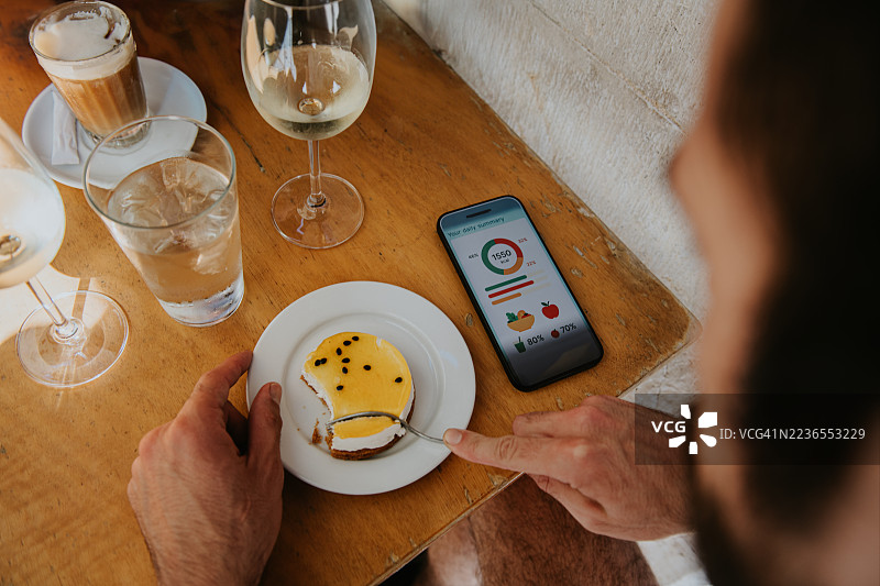 在阳光明媚的日子里，坐在咖啡馆的桌子旁，享受奢华的甜点，同时在智能手机上记录食物和卡路里摄入。图片素材