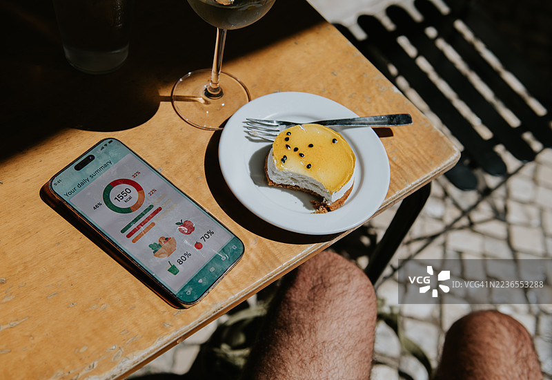 在阳光明媚的日子里，坐在咖啡馆的桌子上享受奢华的甜点，同时在智能手机上记录食物和卡路里摄入。图片素材