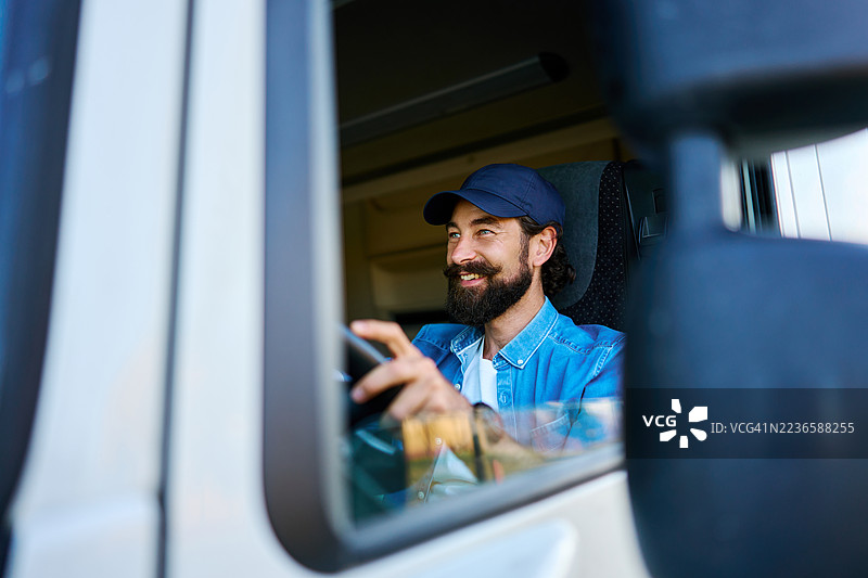 微笑的卡车司机戴着帽子在公路旅行中驾驶车辆图片素材